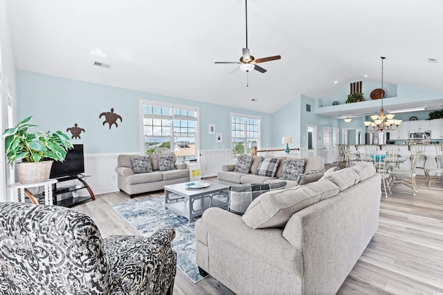 living room with ceiling fan with notable chandelier, lofted ceiling, and light hardwood / wood-style flooring