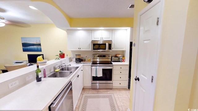 kitchen with appliances with stainless steel finishes, ceiling fan, sink, white cabinets, and light tile patterned flooring