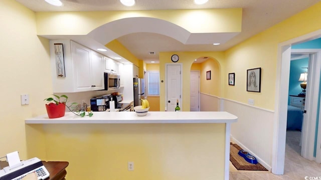 kitchen with kitchen peninsula, white cabinetry, light colored carpet, and stainless steel appliances