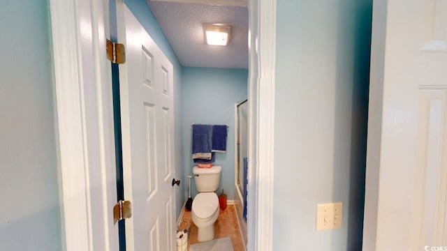 bathroom featuring tile patterned floors, toilet, a shower with shower door, and a textured ceiling