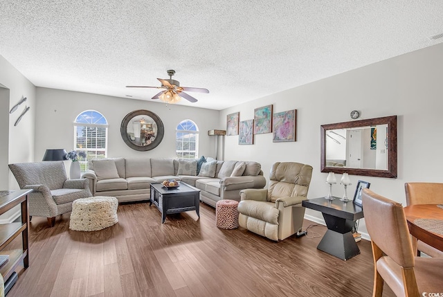 living room featuring ceiling fan, a wealth of natural light, dark hardwood / wood-style floors, and a textured ceiling