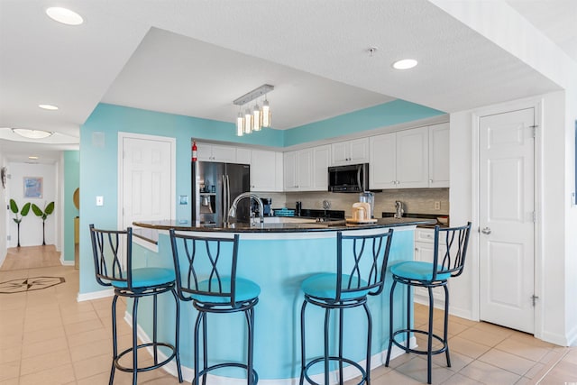 kitchen with decorative backsplash, light tile patterned floors, stainless steel appliances, a center island with sink, and white cabinets