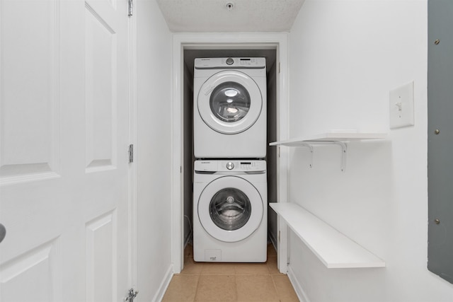 clothes washing area with a textured ceiling, stacked washer and dryer, and light tile patterned floors