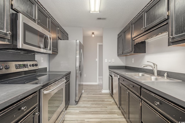 kitchen with appliances with stainless steel finishes, sink, a textured ceiling, and light hardwood / wood-style floors