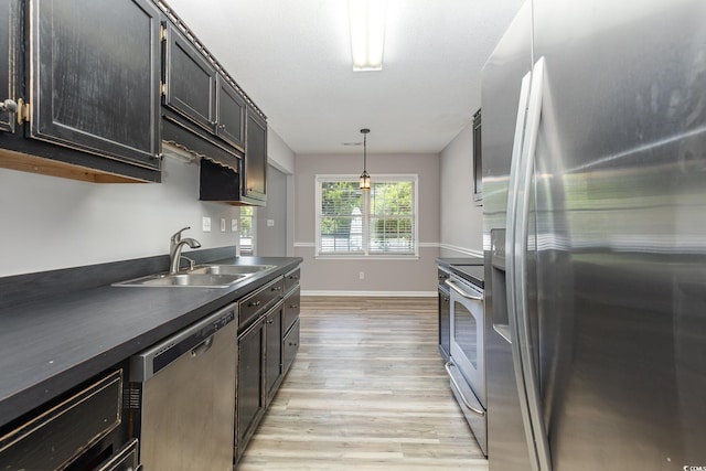 kitchen featuring appliances with stainless steel finishes, decorative light fixtures, sink, light hardwood / wood-style floors, and a textured ceiling