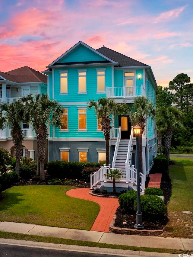 coastal inspired home with a lawn, a balcony, and a porch