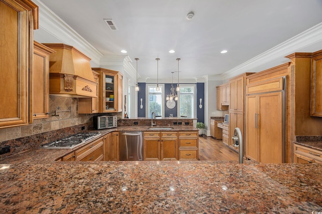 kitchen with custom range hood, light hardwood / wood-style floors, pendant lighting, stainless steel appliances, and sink