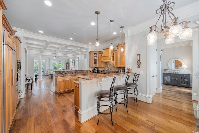 kitchen with a breakfast bar, pendant lighting, sink, kitchen peninsula, and light hardwood / wood-style flooring