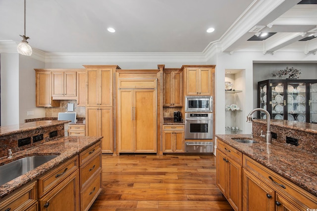 kitchen featuring appliances with stainless steel finishes, hanging light fixtures, light wood-type flooring, beam ceiling, and sink