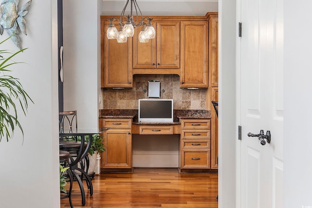 kitchen with built in desk, hanging light fixtures, light hardwood / wood-style flooring, an inviting chandelier, and backsplash