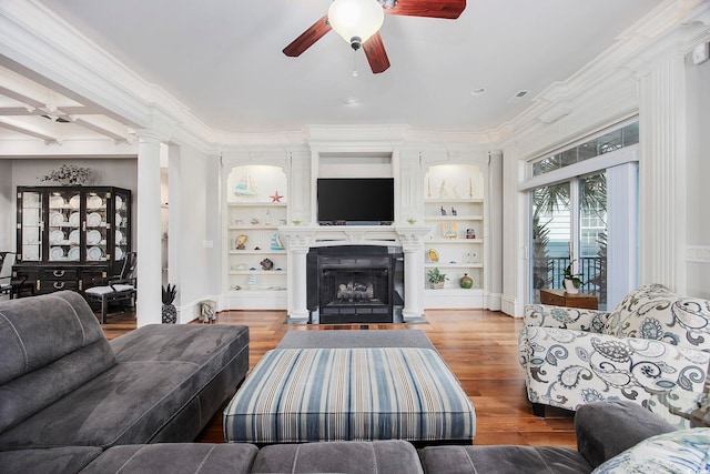 living room featuring ceiling fan, built in shelves, ornamental molding, hardwood / wood-style flooring, and decorative columns