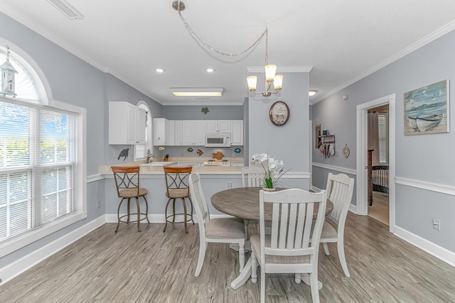 dining room with sink, a chandelier, ornamental molding, and light hardwood / wood-style floors