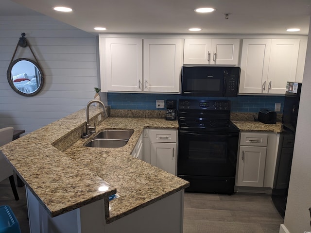 kitchen featuring white cabinetry, kitchen peninsula, black appliances, light stone countertops, and sink