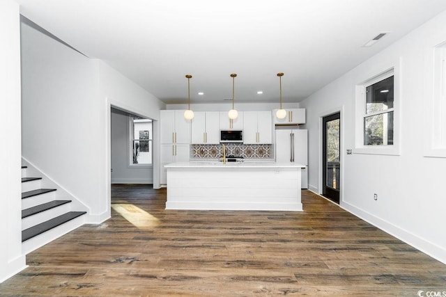 kitchen with a kitchen island with sink, backsplash, dark wood-style floors, freestanding refrigerator, and light countertops