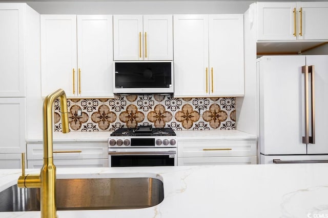 kitchen with light stone counters, freestanding refrigerator, high end stove, white cabinetry, and backsplash