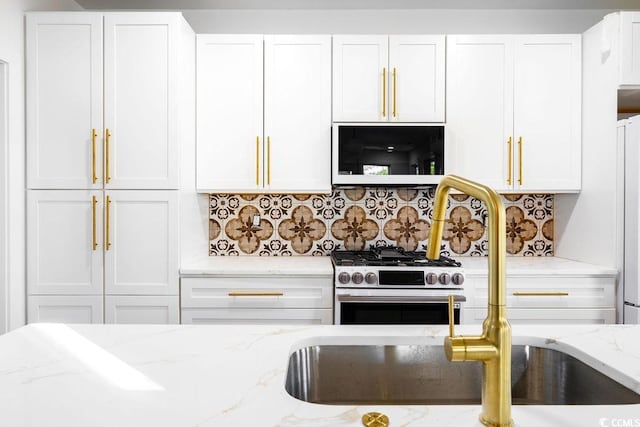 kitchen with decorative backsplash, light stone countertops, stainless steel stove, and white cabinetry