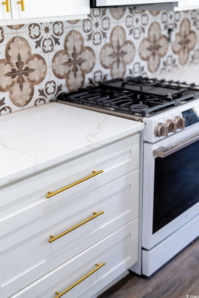 interior details with light stone countertops, white range with gas cooktop, dark wood-style flooring, white cabinets, and tasteful backsplash