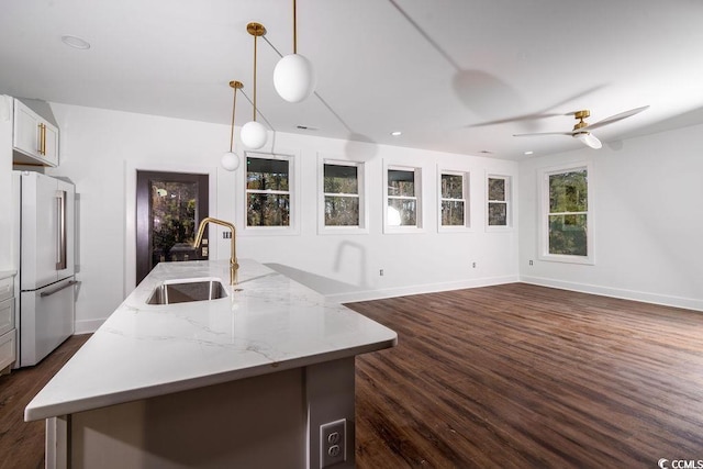 kitchen with dark wood-type flooring, high end fridge, an island with sink, a sink, and baseboards