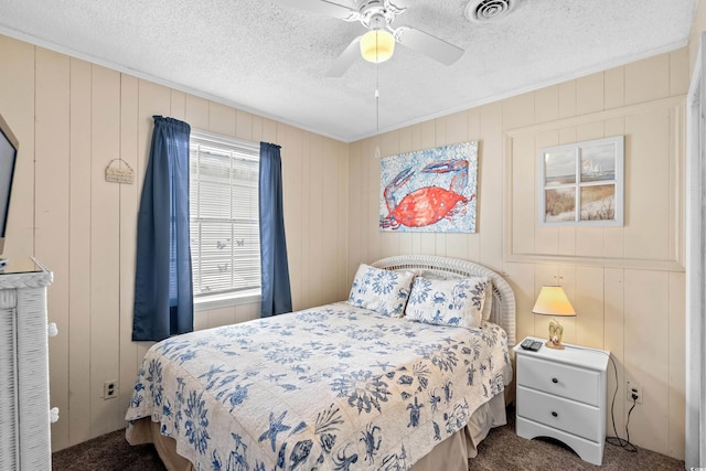 bedroom with wood walls, a textured ceiling, ceiling fan, and dark carpet