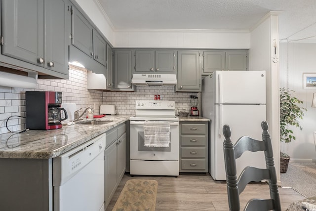 kitchen featuring white appliances, light stone countertops, crown molding, under cabinet range hood, and a sink