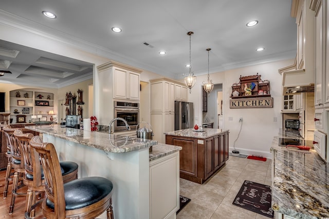 kitchen featuring coffered ceiling, cream cabinets, a center island with sink, built in features, and hanging light fixtures