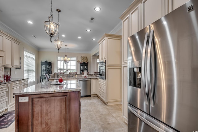 kitchen with appliances with stainless steel finishes, decorative light fixtures, a notable chandelier, cream cabinetry, and a kitchen island