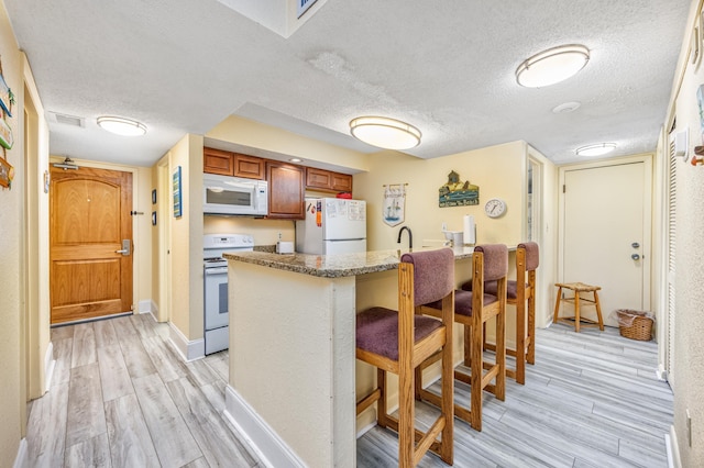 kitchen with white appliances, light wood-type flooring, a textured ceiling, kitchen peninsula, and a breakfast bar area