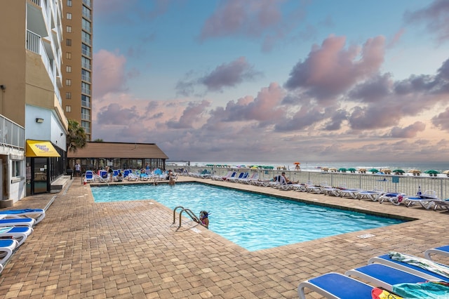 pool at dusk with a water view and a patio