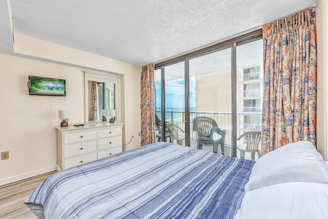 bedroom featuring light hardwood / wood-style floors, expansive windows, access to outside, and a textured ceiling