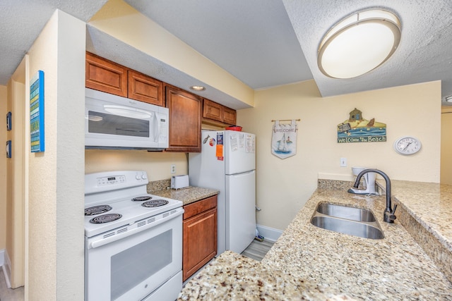 kitchen with white appliances, sink, a textured ceiling, kitchen peninsula, and light stone countertops