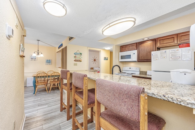 kitchen featuring light hardwood / wood-style flooring, white appliances, light stone counters, and a textured ceiling