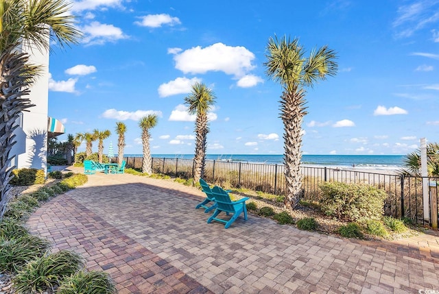 view of patio / terrace with a water view, fence, and a view of the beach