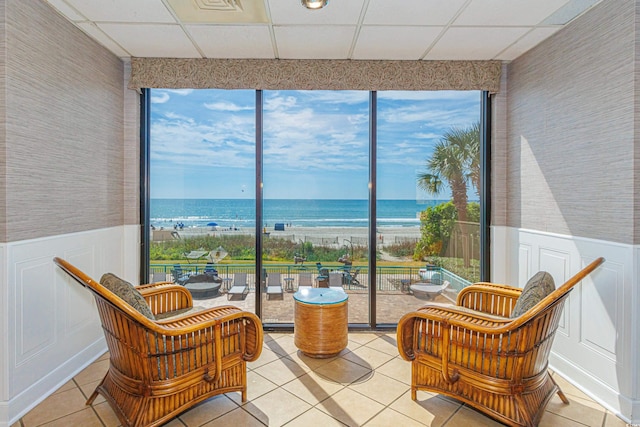 living area with a drop ceiling, tile patterned floors, a beach view, and a water view