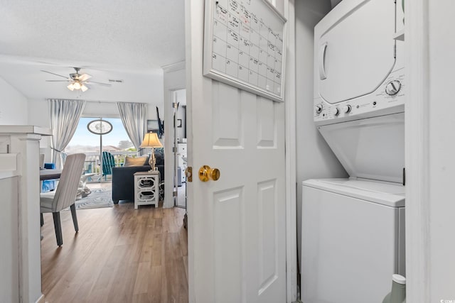laundry room featuring ceiling fan, a textured ceiling, light wood-type flooring, and stacked washer and dryer