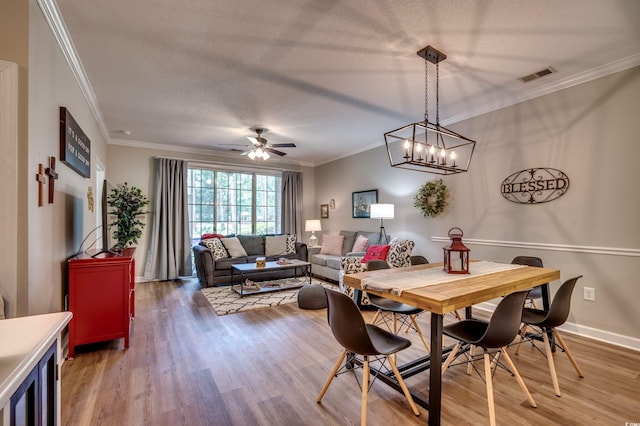 dining space with a textured ceiling, wood-type flooring, ornamental molding, and ceiling fan