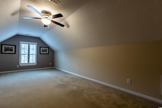 additional living space with carpet, a textured ceiling, vaulted ceiling, and ceiling fan