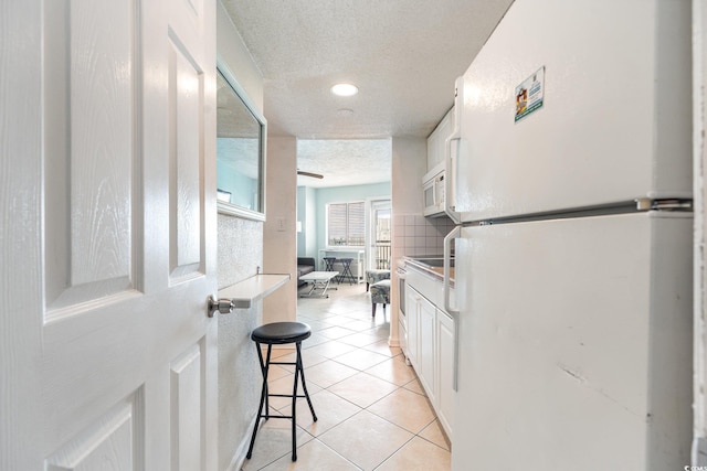 kitchen featuring white appliances, light tile patterned floors, a textured ceiling, white cabinetry, and a kitchen breakfast bar