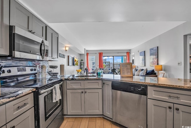 kitchen featuring gray cabinets, stainless steel appliances, light hardwood / wood-style floors, backsplash, and light stone counters