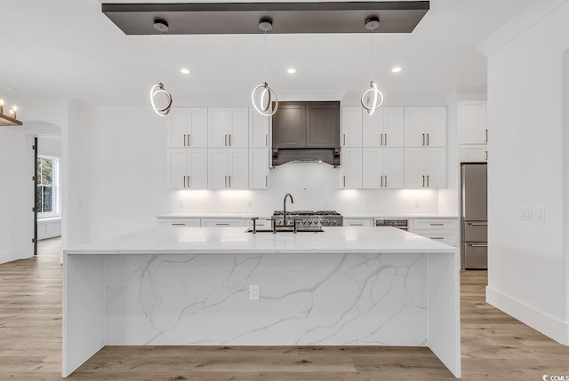 kitchen featuring sink, a kitchen island with sink, decorative light fixtures, and light wood-type flooring