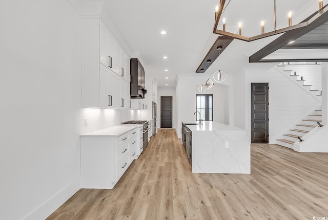 kitchen with white cabinetry, light stone counters, sink, and light wood-type flooring