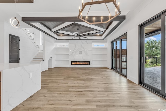 unfurnished living room with light wood finished floors, stairs, a ceiling fan, built in shelves, and a chandelier