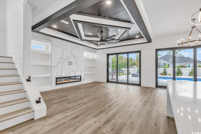 unfurnished living room featuring wood-type flooring, ceiling fan with notable chandelier, built in features, a tray ceiling, and a tile fireplace