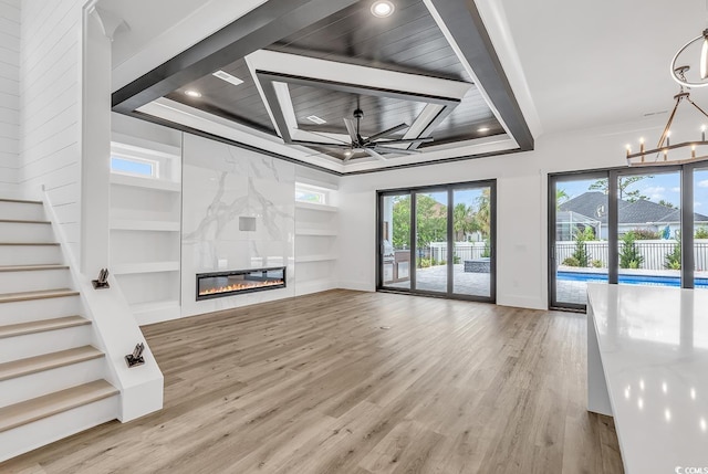 unfurnished living room featuring built in features, a chandelier, healthy amount of natural light, wood finished floors, and recessed lighting