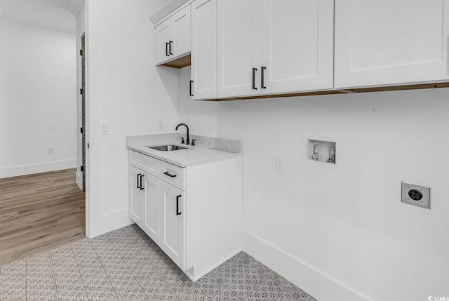 washroom with hookup for a washing machine, hookup for an electric dryer, sink, light hardwood / wood-style floors, and cabinets