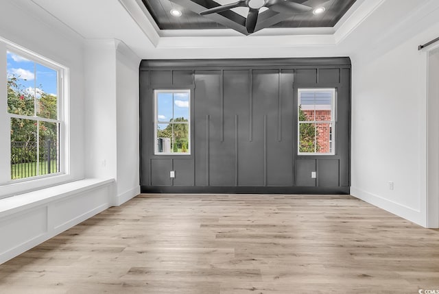 unfurnished room with ornamental molding, healthy amount of natural light, a ceiling fan, wood finished floors, and a decorative wall