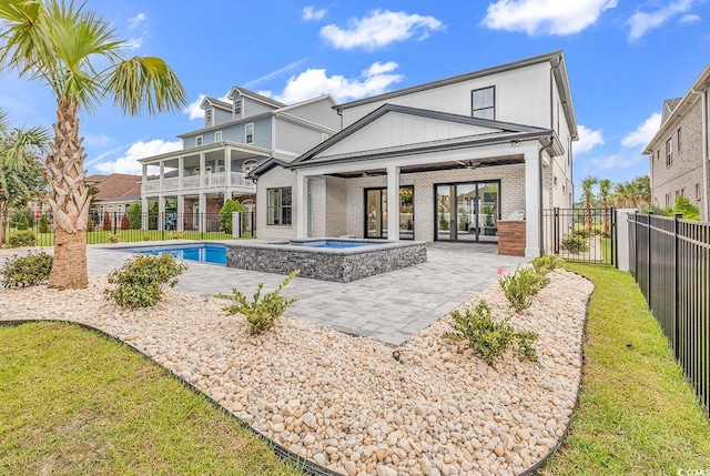 rear view of house with a balcony, a swimming pool with hot tub, a patio area, and a lawn