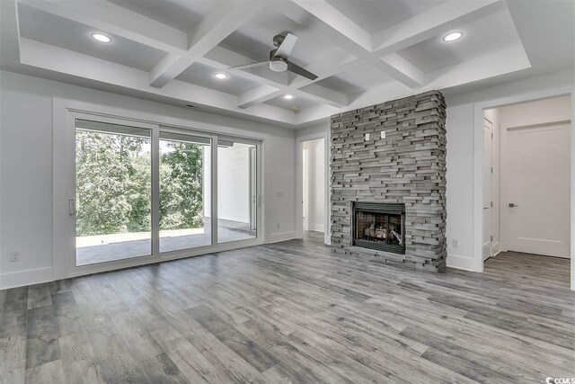 unfurnished living room featuring beam ceiling, ceiling fan, light wood-type flooring, a stone fireplace, and coffered ceiling