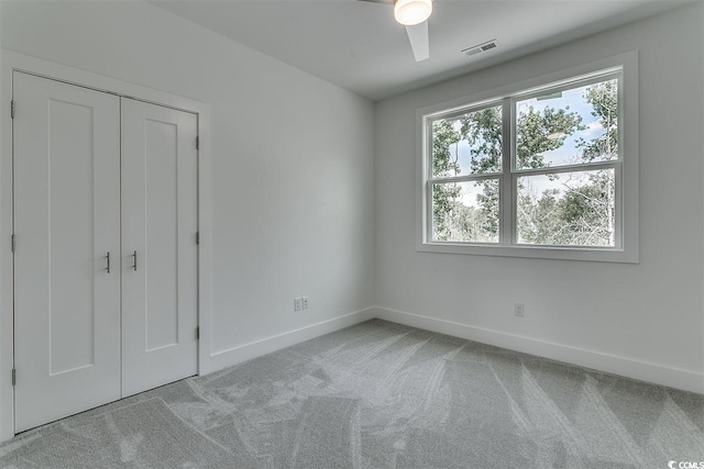 unfurnished bedroom featuring a closet, light colored carpet, and ceiling fan