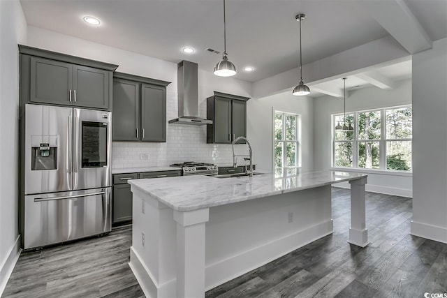 kitchen featuring an island with sink, stainless steel appliances, wall chimney exhaust hood, decorative light fixtures, and dark wood-type flooring