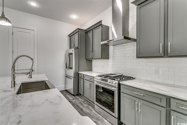 kitchen featuring wall chimney exhaust hood, hanging light fixtures, sink, light stone countertops, and appliances with stainless steel finishes